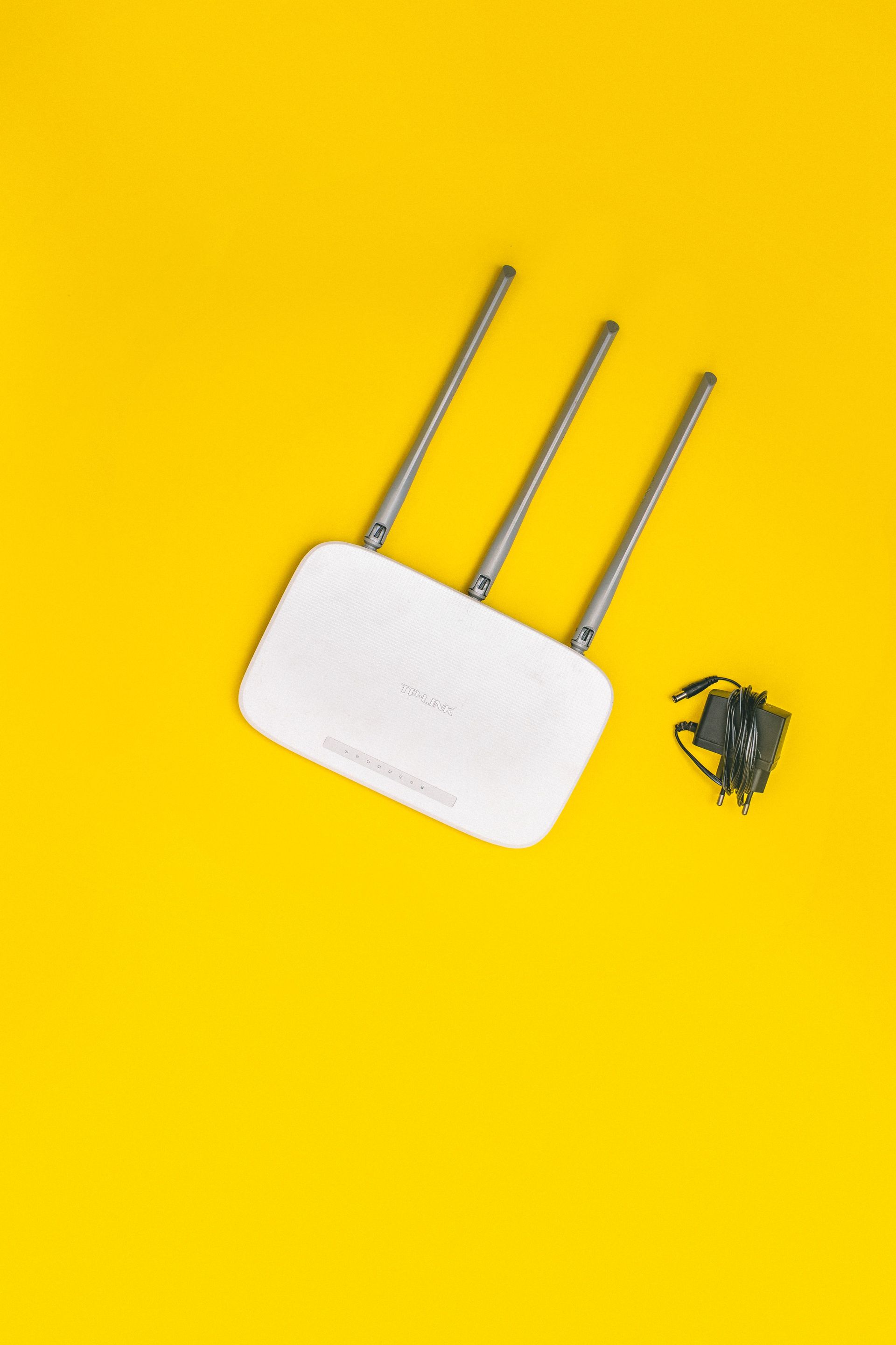 White router with three antennas and cables on bold yellow background, ideal for tech concepts.