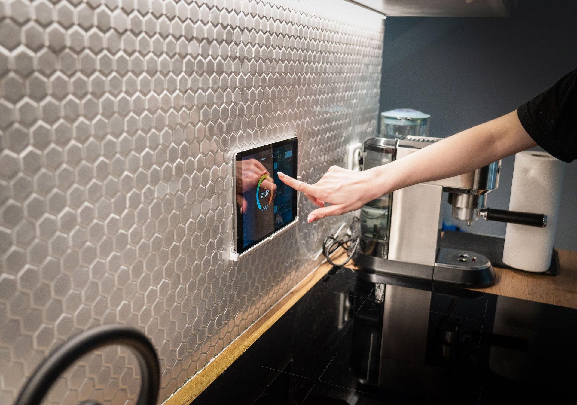 A modern kitchen with a touchscreen smart home control panel integrated into a hexagon-patterned wall.